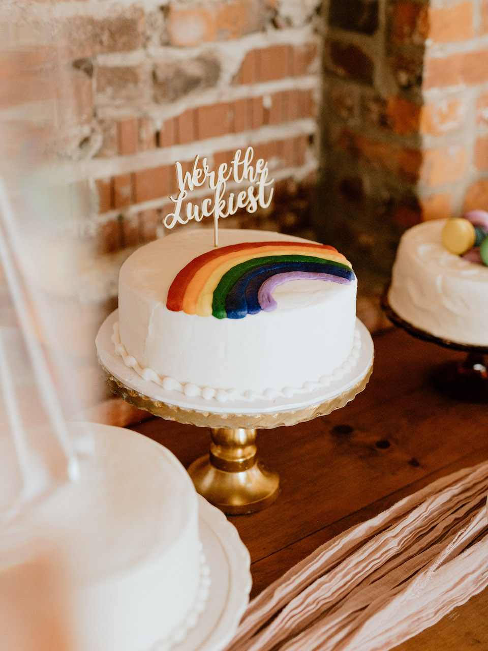 Single tier white wedding cake with a frosting rainbow and a sign saying we're the luckiest