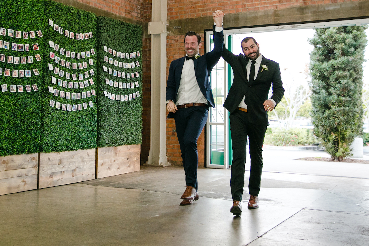 Two grooms holding hands walking into their wedding reception at BRICK in San Diego
