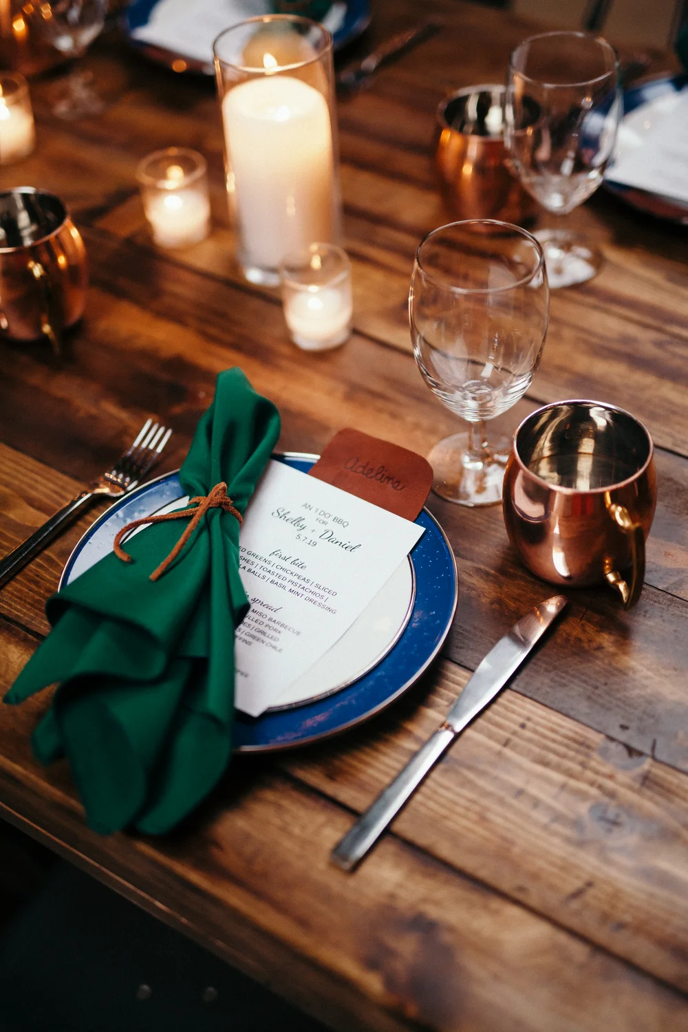 Holiday table setting with blue plate and green napkin tied with a leather bow