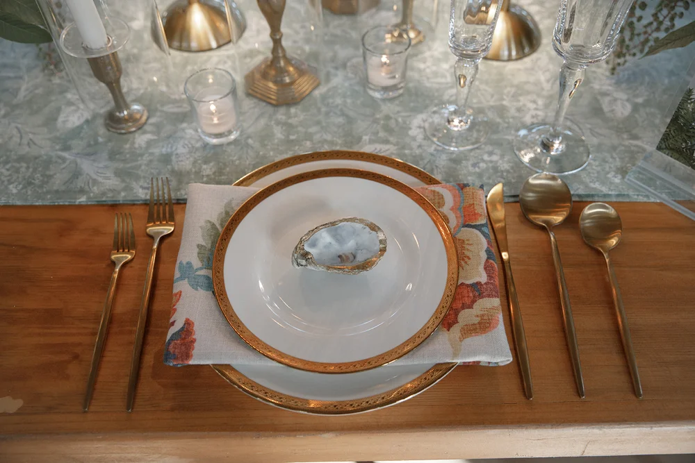 Tablescape design with gold-rimmed plates and oyster name cards at NOLA-inspired open house planned by 828 Planning