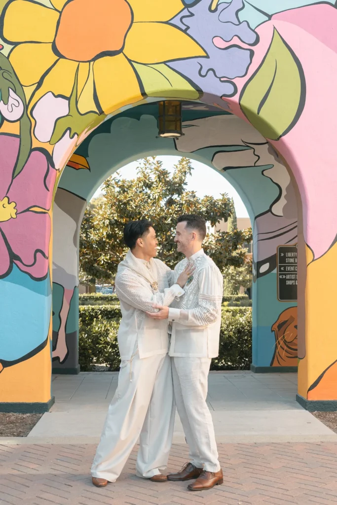Grooms smiling at each other in front of a colorful mural in San Diego